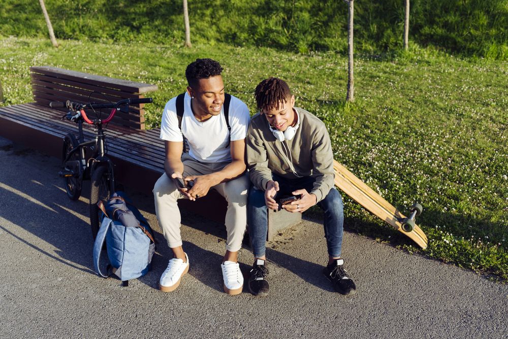 Young Black men sitting on bench with smartphone