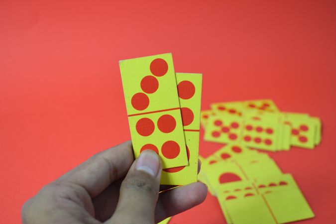 Person holding two domino cards over red table