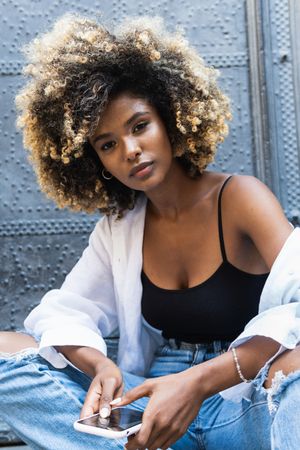 Young Black woman speaking on smartphone while sitting near building