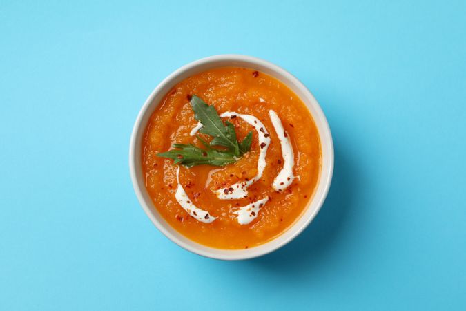 Top view of bowl of pumpkin soup on blue table
