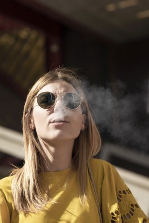 Stylish young woman in sunglasses smoking