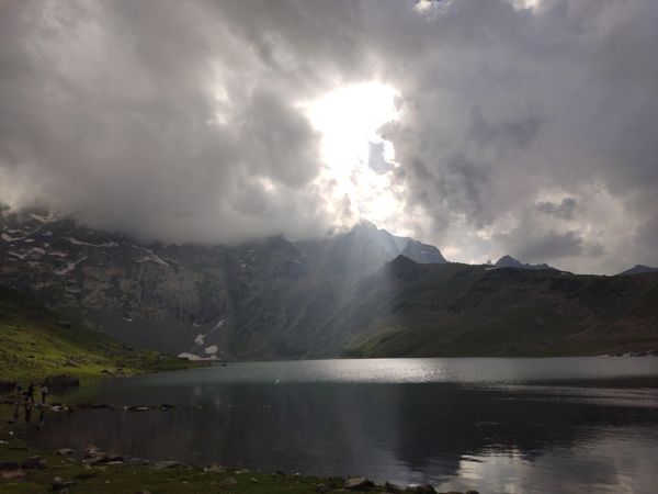 Sunrays out of cloudy sky on calm lake near mountains