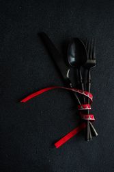 Dark knife and fork on dark background tied with festive red ribbon