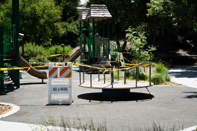 Caution and closed signs around city playground with merry-go-round and slides