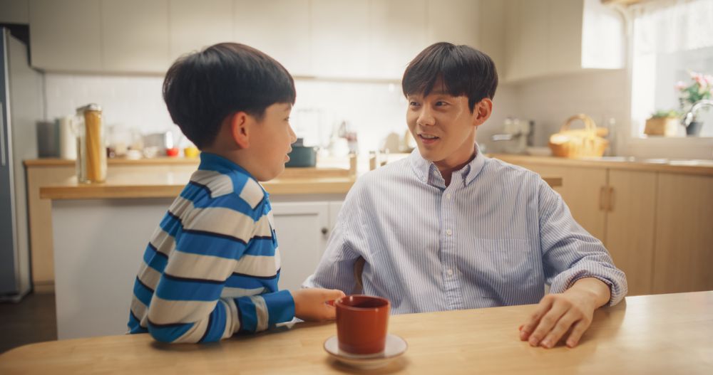 Portrait of Fatherly Love: Korean Young Man and his Son Talking, Joking Around, Bonding Together While Sitting at Home.