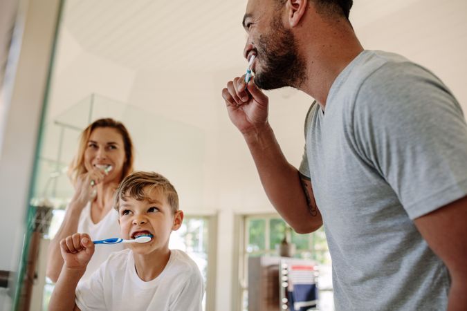 Cute little boy brushing teeth with his father and mother in bathroom