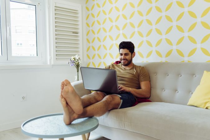 Young cheerful male with laptop sitting on sofa