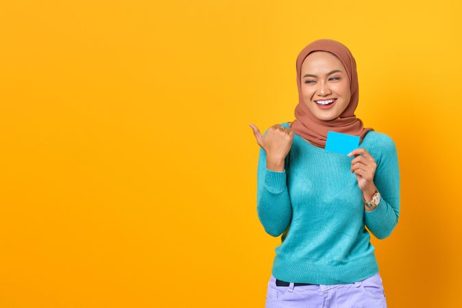 Muslim woman looking happy with credit card and pointing away
