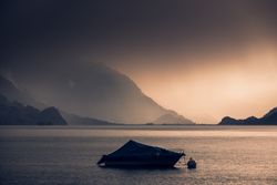 Lonely yacht in gray water with dark mountains under cloudy sky