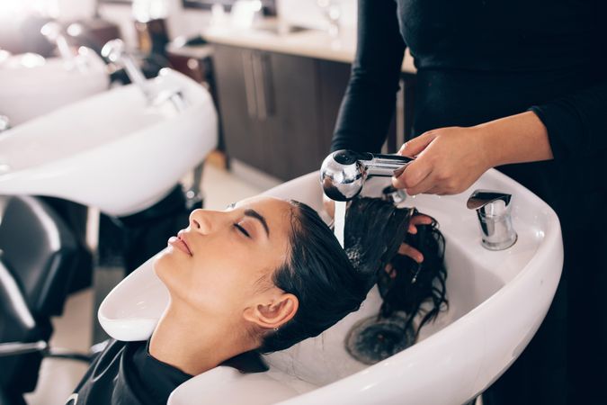 Close up of female hairdresser rinsing customer’s long hair
