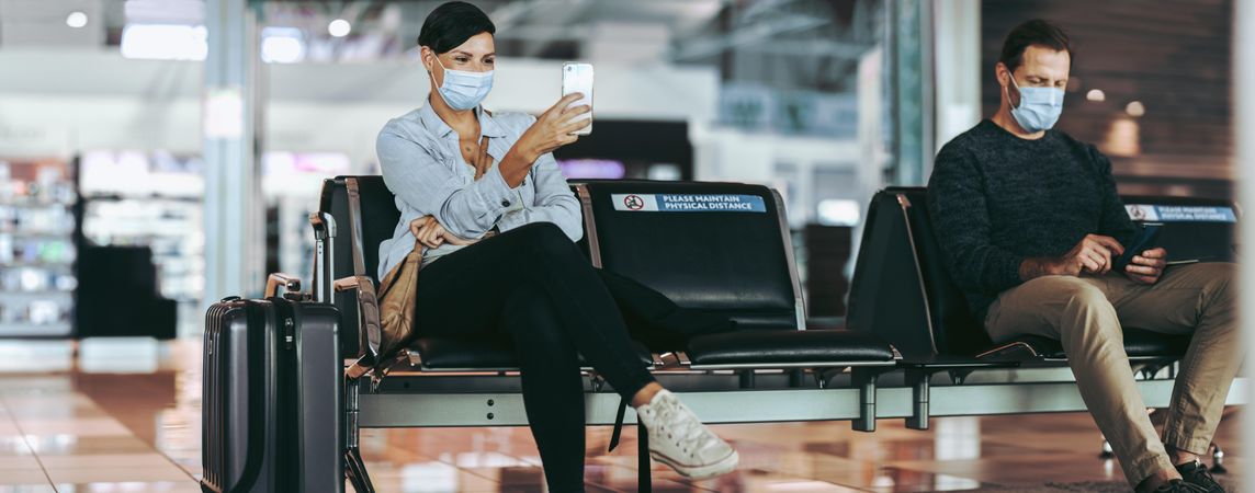 Man and woman traveler sitting apart maintaining social distance at airport