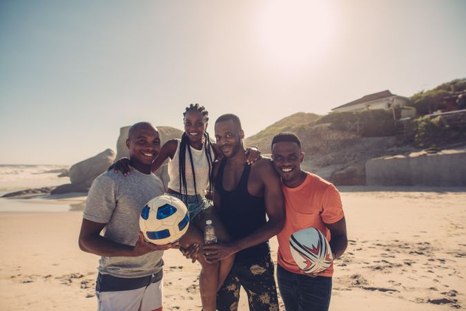 Young friends standing together on beach soccer ball smiling and looking at camera