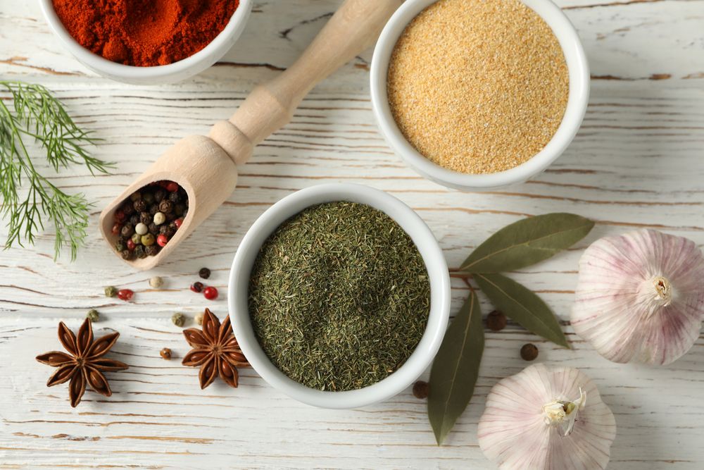 Top view of wooden scoop full of peppercorn with bowls of spice