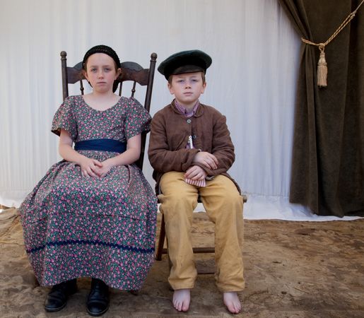 Two children in period garb sitting for historical Civil War reenactment