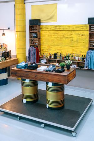 Interior of empty vintage apparel store with clothes over wooden counter supported by fuel barrels