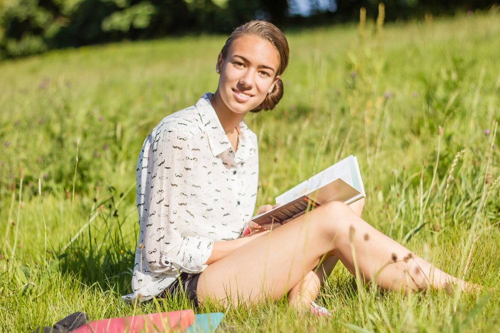young student reading a book in the park