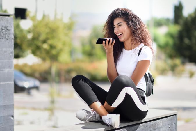 Arab woman chatting on phone and laughing sitting outdoors