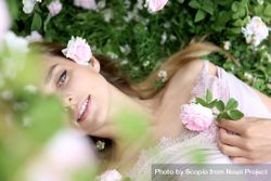 Woman in light dress lying on grass between flowers bxmgr0