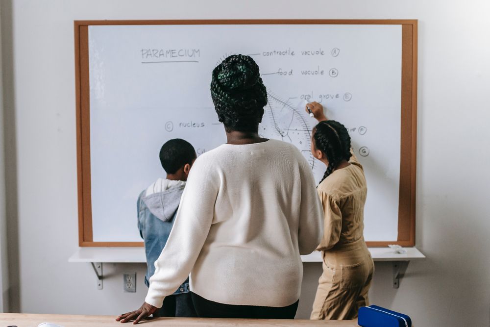 Back view of a teacher supervising students while solving math problem on light bard
