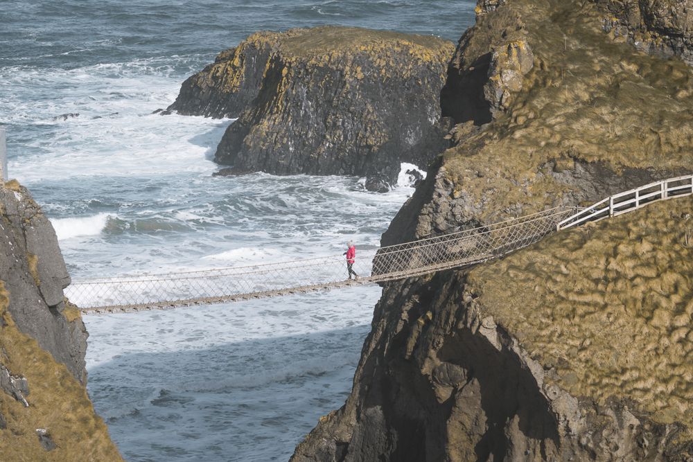Tourist walking on rope bridge suspended between cliffs in Northern Ireland