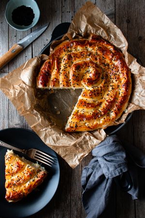 From above crop cook holding hot baking dish with fresh puff pastry and serving piece of borek on plateFaceless person serving homemade borek on wooden table