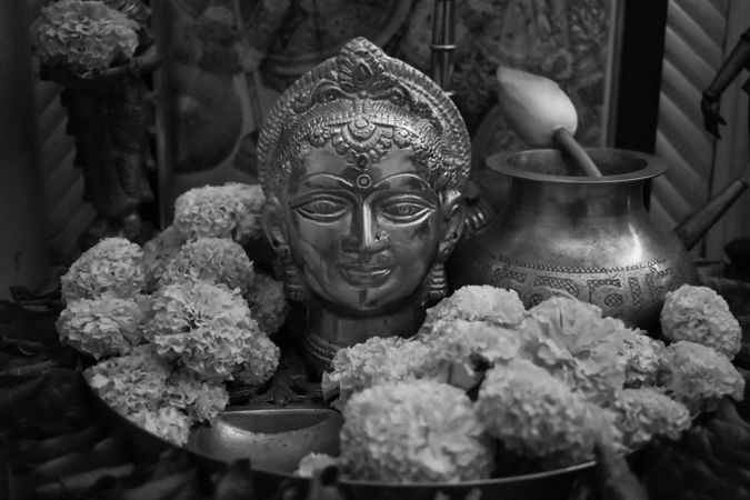 Grayscale photo of Buddha statue surrounded by marigold flowers on tray