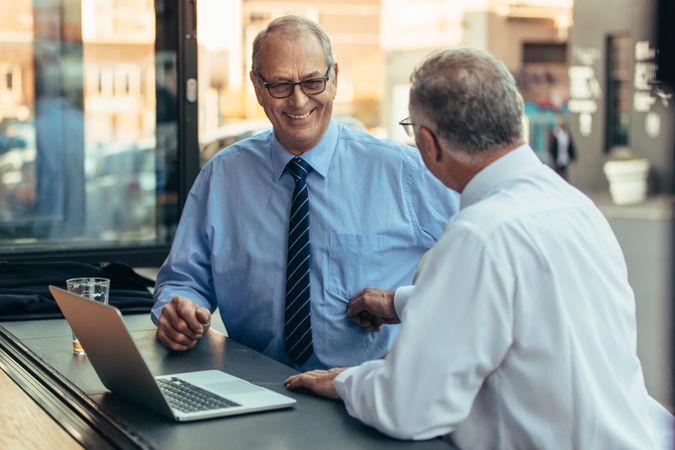 Mature businessmen at cafe counter with laptop discussing collaboration deal
