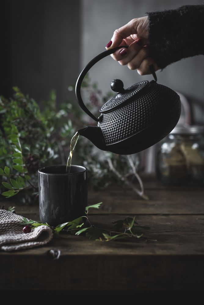 Woman pouring green tea in mug on wooden table with green herb
