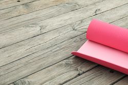 Pink yoga mat on wooden background, space for text