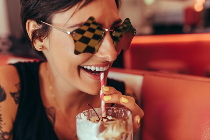 Close up of a smiling  woman in star shaped fancy eyeglasses drinking a milkshake