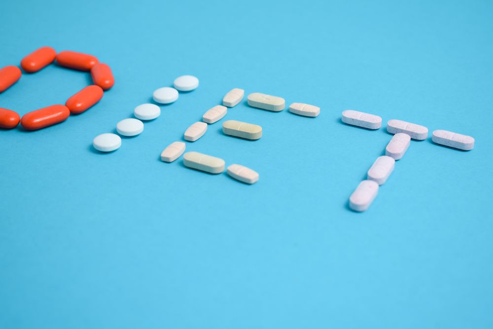 Multiple pills spelling the word "DIET" on blue table with copy space