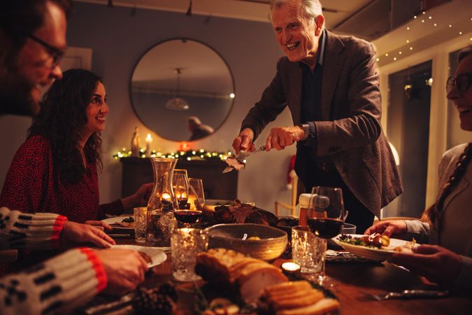 Older man serving food to his family sitting at dinner table on Christmas eve