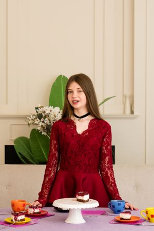 Teen girl in red lace dress smiling beside dessert table.