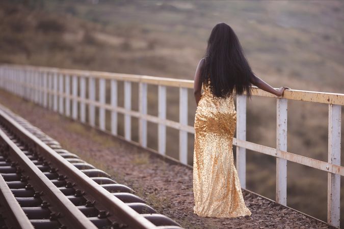 Woman in golden dress standing beside train rail