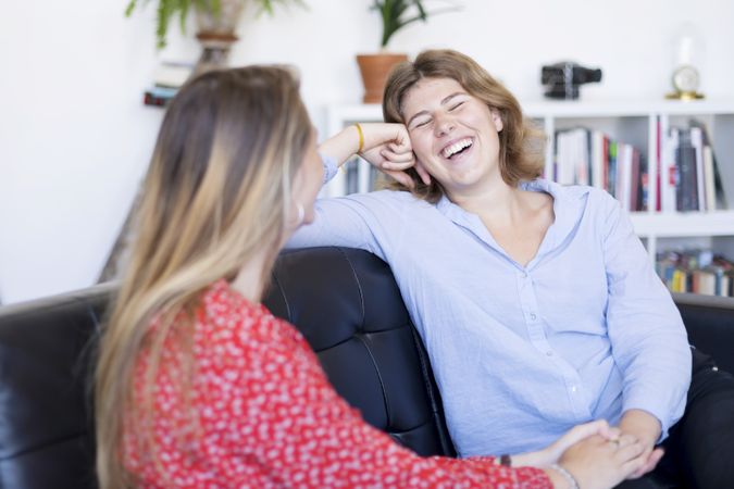 Two friends laughing on a sofa in the living room at home