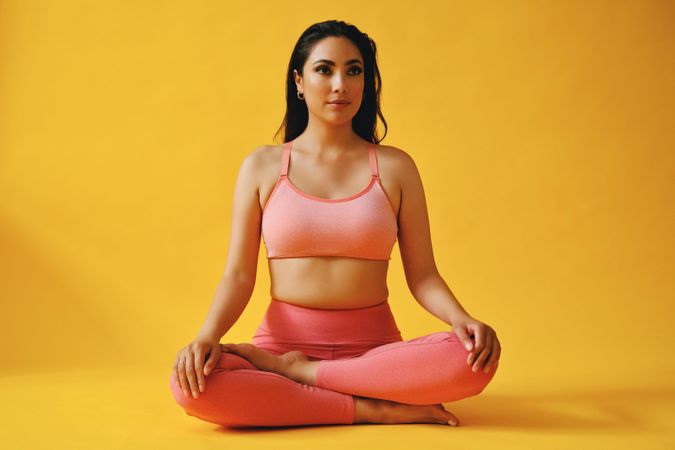 Hispanic female sitting in yoga pose in yellow studio shoot