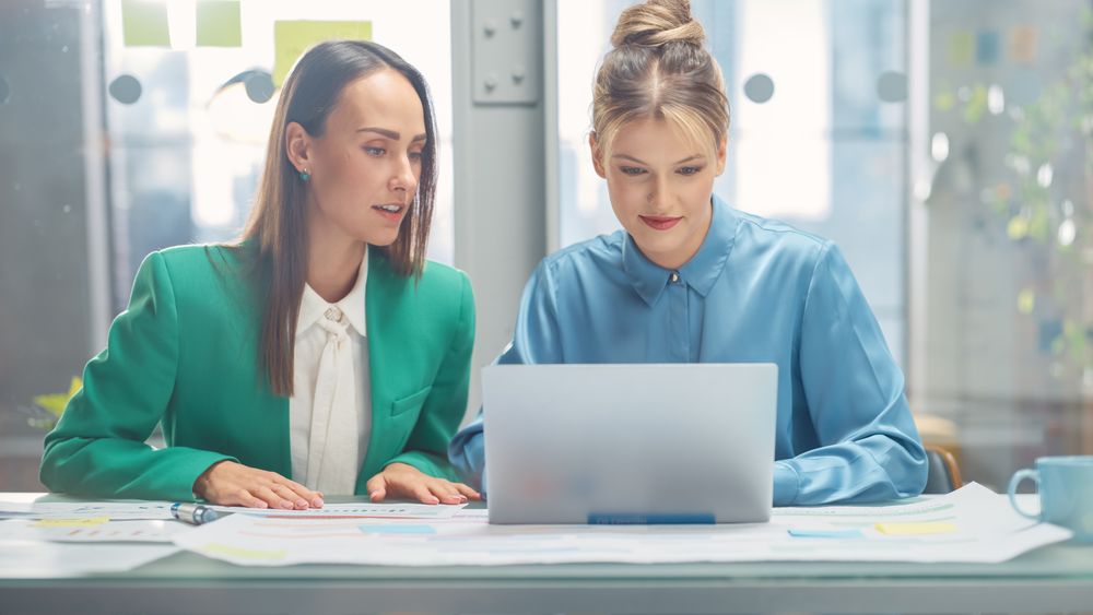 Two White Females Have a Discussion in Meeting Room Behind Glass Walls in an Agency.