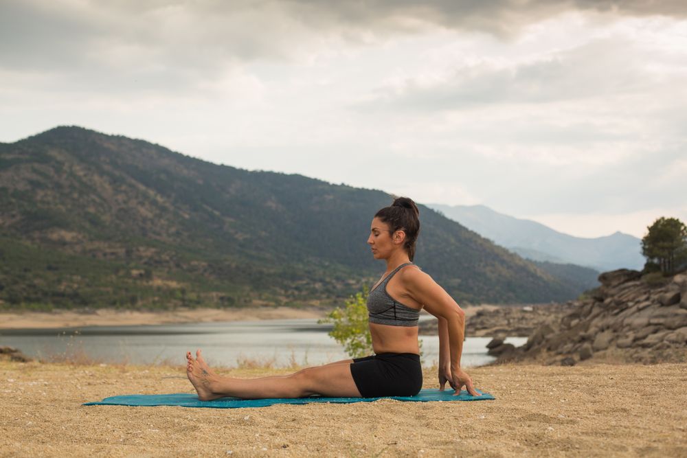 Woman practicing yoga outdoors near water