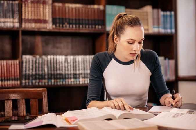 Female student taking notes from book for school assignment