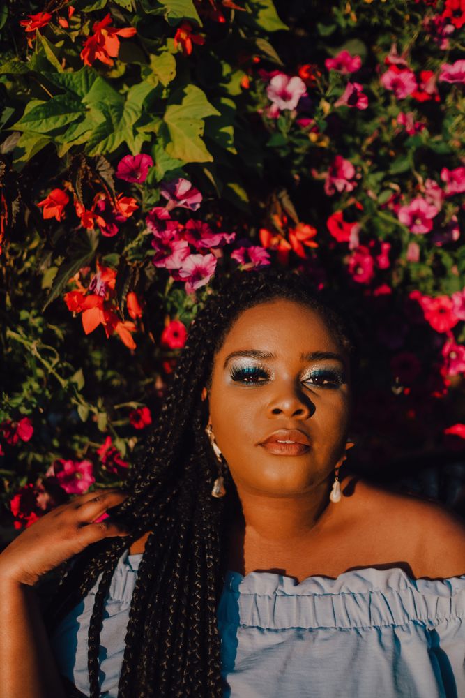 Joyful trendy Black woman standing beside blossomed tree