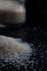 granulated sugar spilling from a glass jar onto a dark surface
