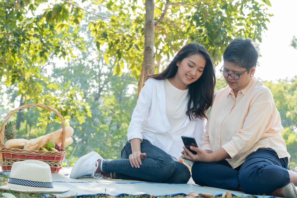 Older woman and her daughter on smartphone in public park