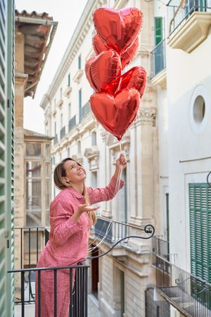 Positive female with red balloons on balcony of multistory build