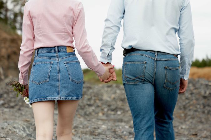 Back view of man and woman holding hands walking near woods