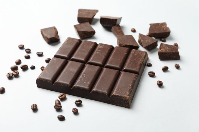 Chocolate bar and coffee seeds on light background
