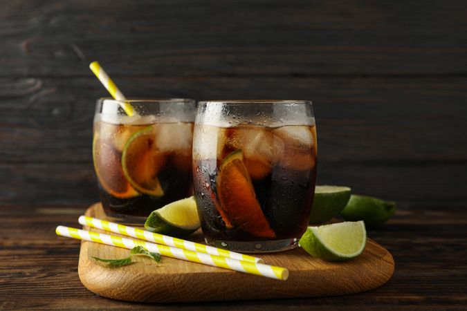 Glasses with ice cola, lime slices and tubules on wooden background