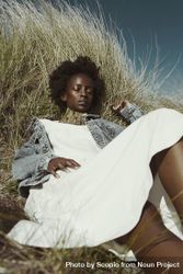 Woman in light dress and denim jacket laying on brown grass bDmwE0