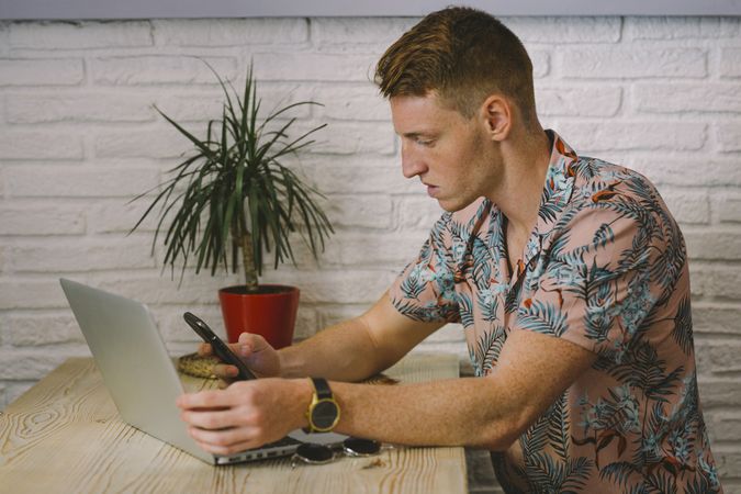 Man talking on smartphone while browsing laptop