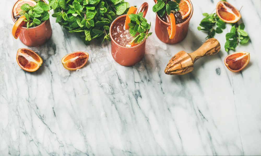 Cold Moscow mules with blood oranges and citrus reamer on marble table