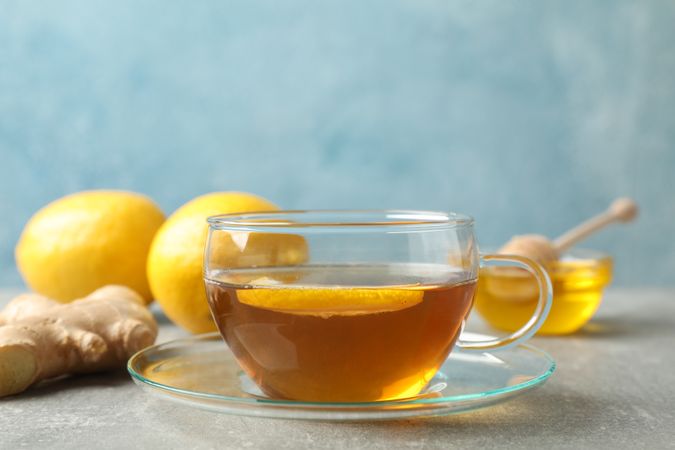 Cup of tea, lemon, honey and ginger on grey background, space for text
